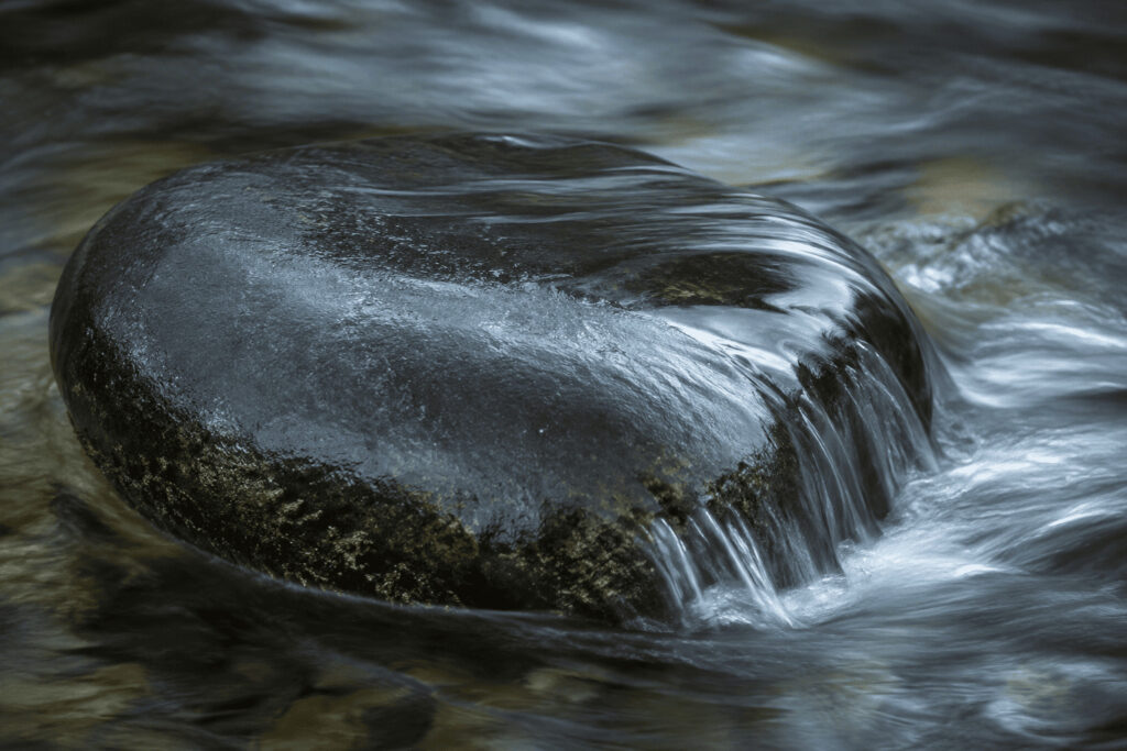 Water flowing over smooth dark stone — a visual metaphor for Wu Wei and effortless action in Taoism